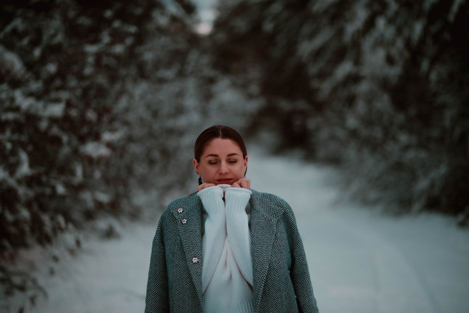 A serene moment captured of a woman in a stylish coat amidst a snowy forest setting.