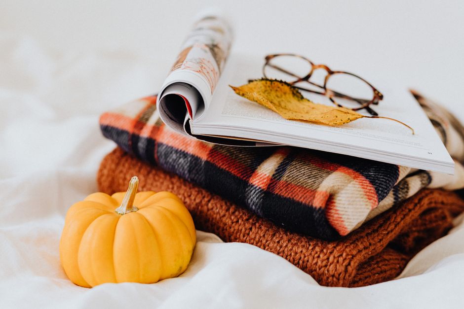 A warm, cozy still life featuring a plaid blanket, small pumpkin, and reading glasses on a