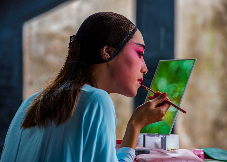 A woman carefully applying lipstick, reflecting artfully in a mirror with a blurred backgr
