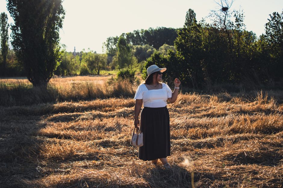 A woman in a summer outfit walks through a sunlit field, exuding warmth and tranquility.