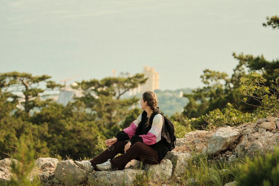 A young woman sits on a rocky hilltop, enjoying a scenic view of nature.