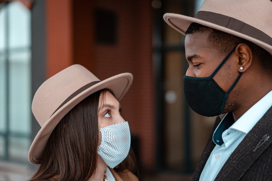 Close-up of a diverse couple in conversation, wearing face masks and stylish fedora hats outdoors.