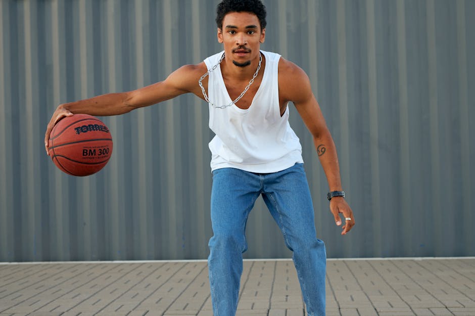 Athletic young man dribbling a basketball outdoors in jeans and tank top.