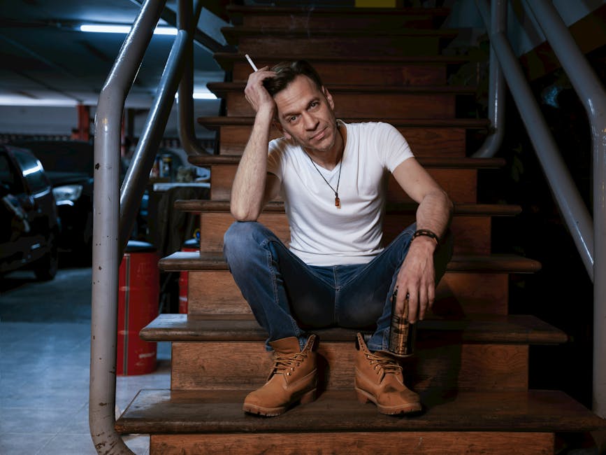Man in casual attire sitting on indoor stairs with a thoughtful pose.