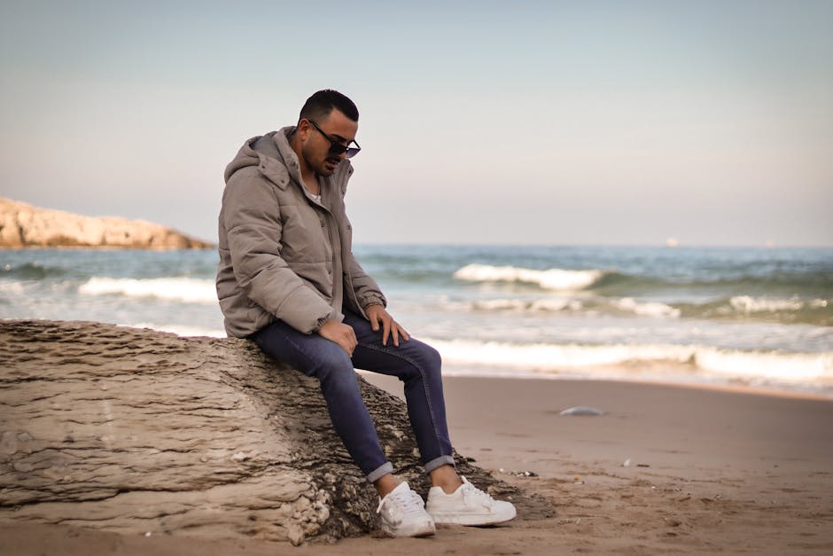 Man in winter attire sitting on a rock by the seaside, conveying a relaxed mood.
