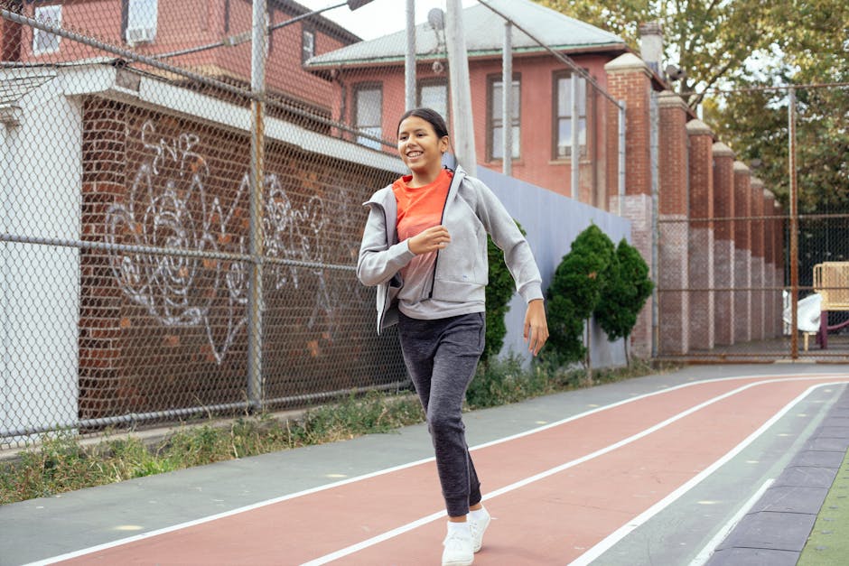 Full body of happy Latin American schoolgirl in sportswear toothy smiling while jogging on stadium