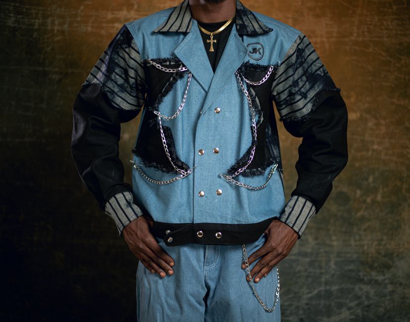 Portrait of man in denim jacket with chains, showcasing modern fashion style.