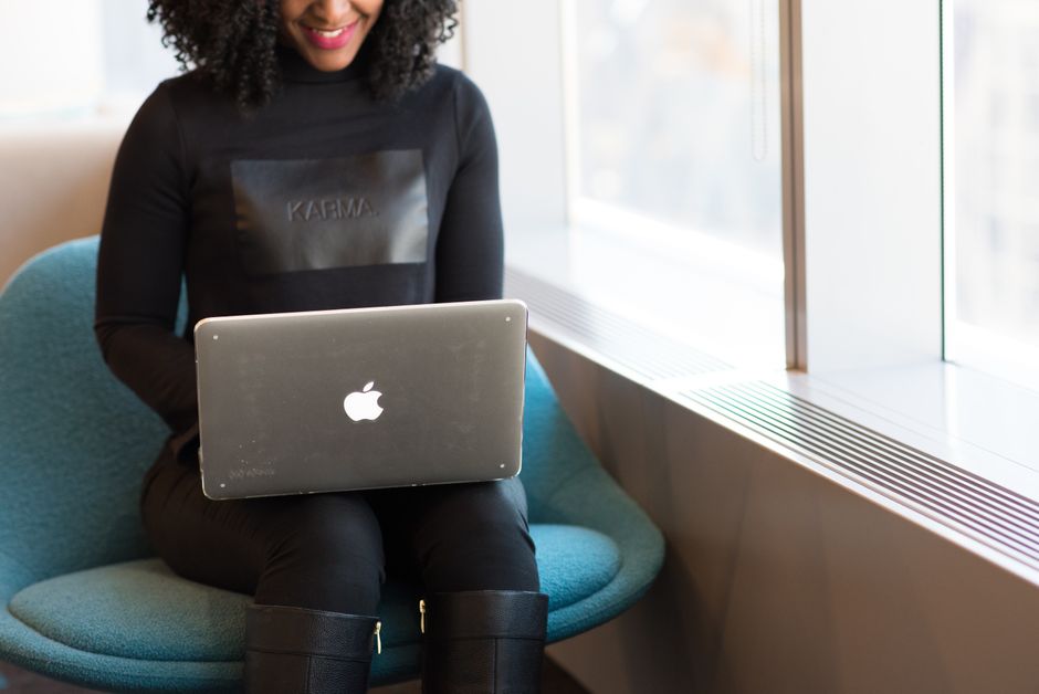 Smiling woman working on a laptop seated by a window in a modern office. Ideal for remote work themes.