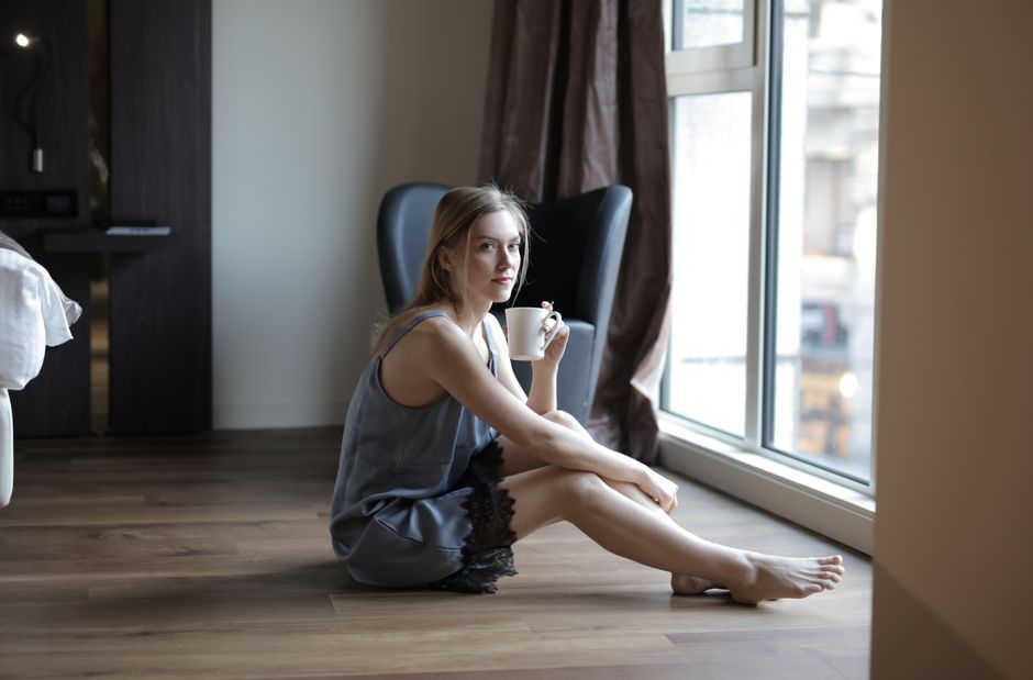 A woman in pajamas relaxing with a coffee cup near a window indoors.