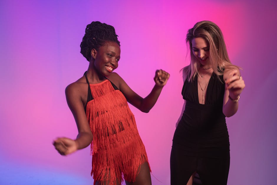 Two women enjoying a dance party with vibrant colored lights, dressed in elegant party outfits.