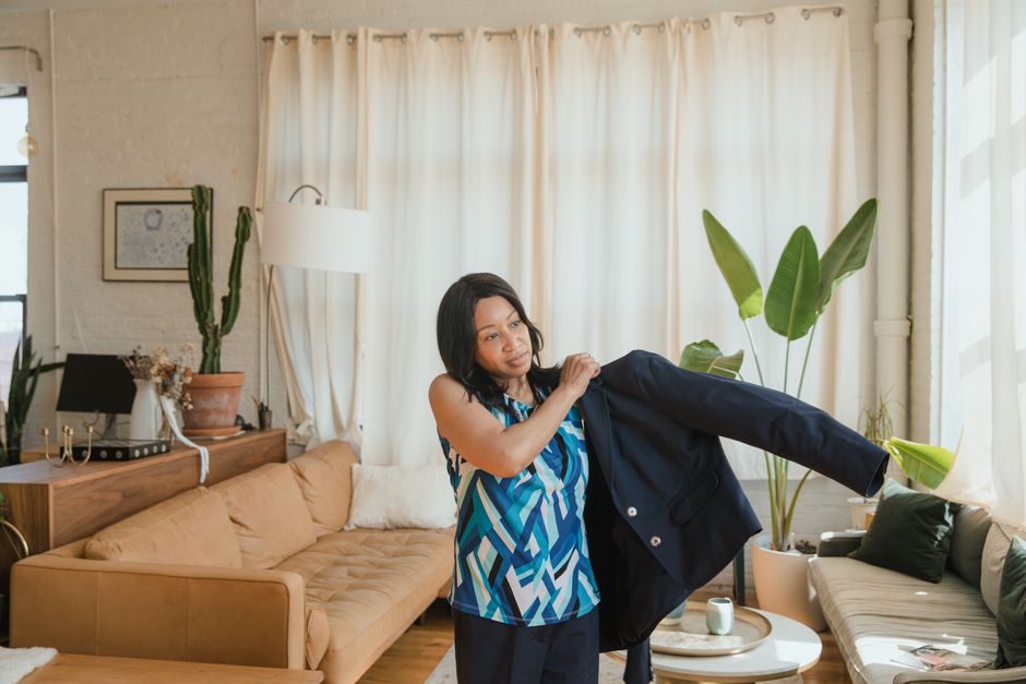 A confident adult woman putting on a black coat in a modern, stylish living room setting.