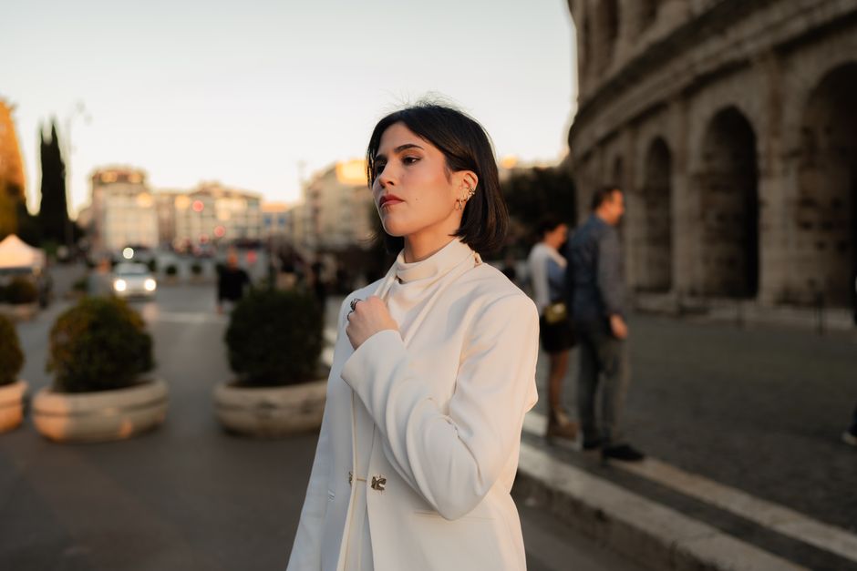 Stylish woman in white coat poses near the Colosseum during a beautiful sunset in Rome.