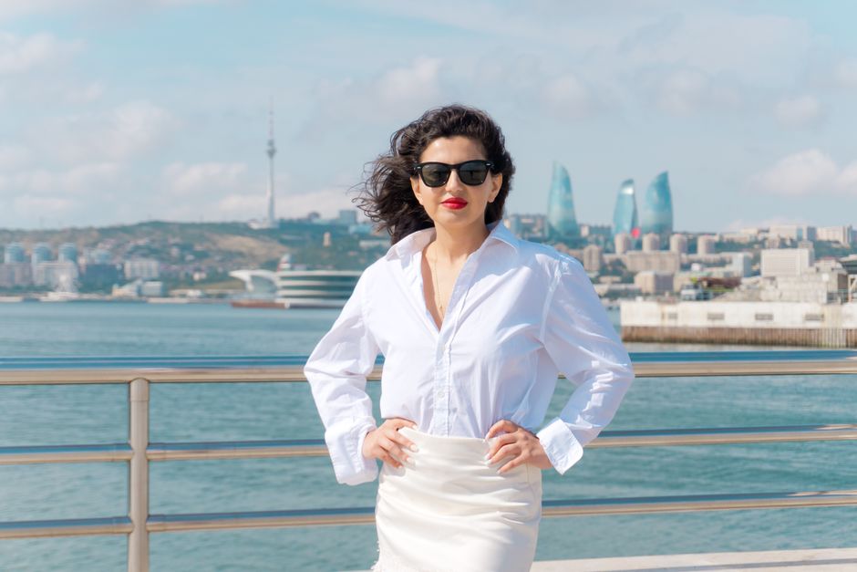 Elegant woman in sunglasses posing at Baku Bay with Flame Towers view.