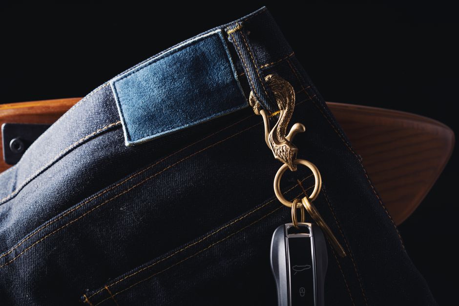 Close-up of denim jeans with a keychain featuring a carved eagle and car key. Stylish accessory detail.