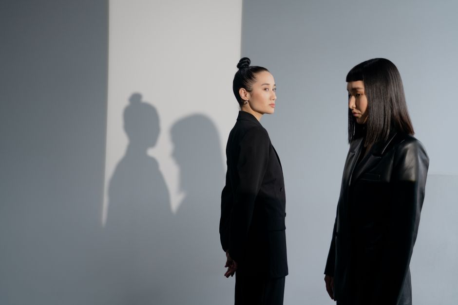 Two fashionable Asian women in black outfits posed in a minimalistic studio setting.