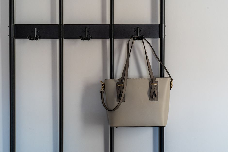 Stylish grey leather purse with gold details hanging on a modern black hook against a minimalist backdrop.