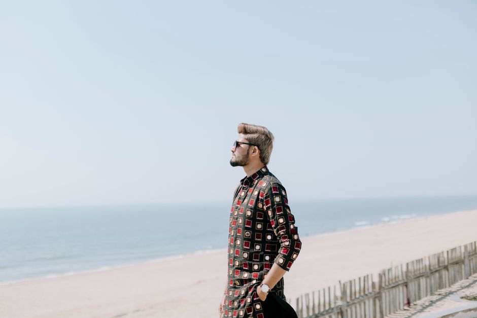 Fashionable man with sunglasses strolling along a bright beach on a sunny day, exuding style and leisure.