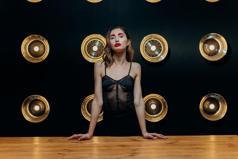 Elegant woman in a black top poses in front of artistic lighting. Studio photography with bold makeup.