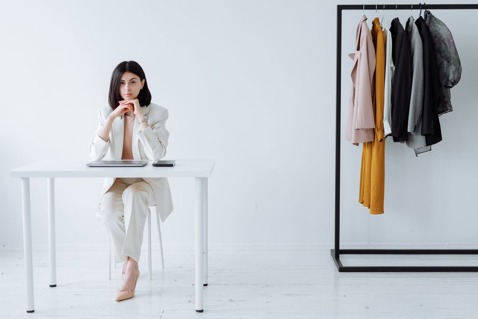 Modern businesswoman sitting at desk with clothing rack, embodying fashion and professiona