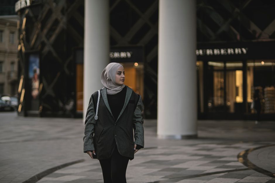 Woman in stylish attire with hijab near Burberry and luxury shops.