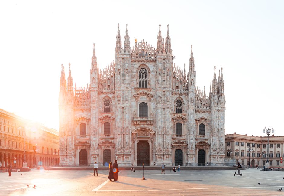 Stunning sunrise view of the Milan Cathedral with few people around, highlighting its gothic architecture.
