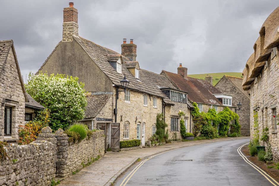 Quaint stone cottages line a quiet road in an idyllic English village setting.