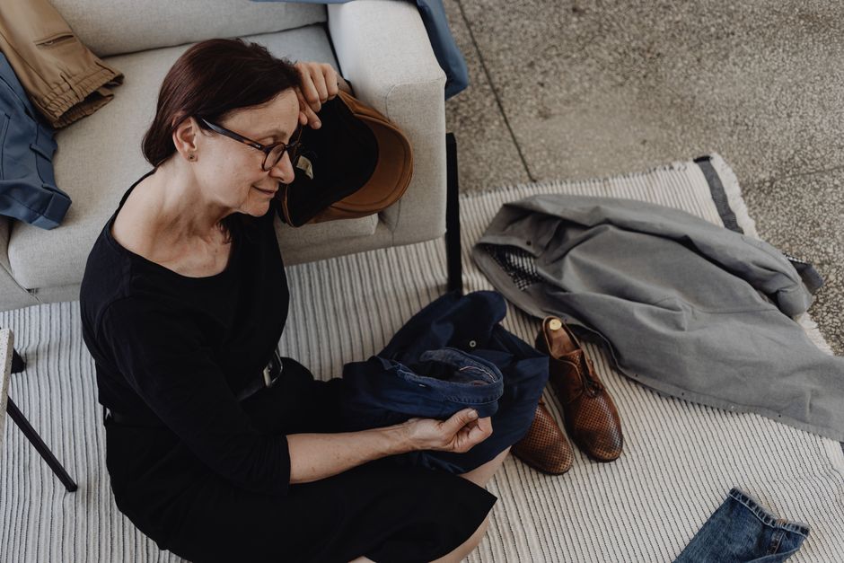 Senior woman seated on floor, deep in thought, surrounded by clothes, depicting contemplation and solitude.
