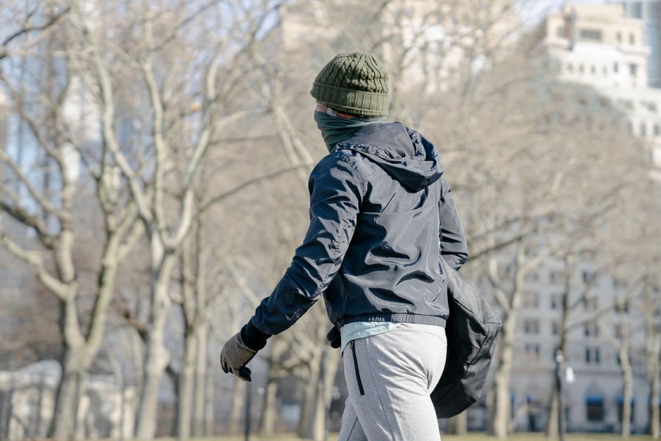 Side view of anonymous male in warm clothes walking with bag near leafless trees on street
