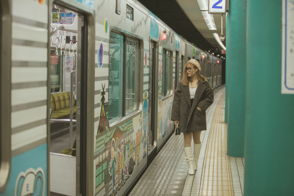 Stylish woman in a checkered blazer and white boots near a graffiti subway train.