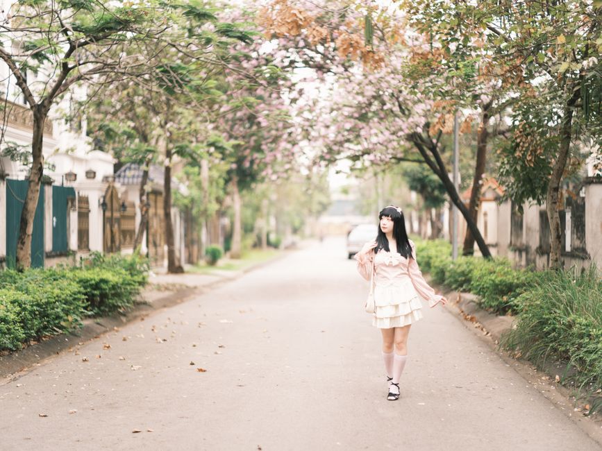 A young woman in a pink dress walking on a tranquil, tree-lined street in spring.
