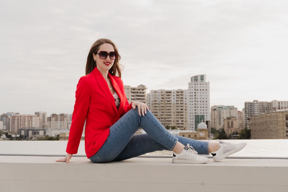 Stylish woman in red blazer and jeans enjoys city view in Baku, Azerbaijan.