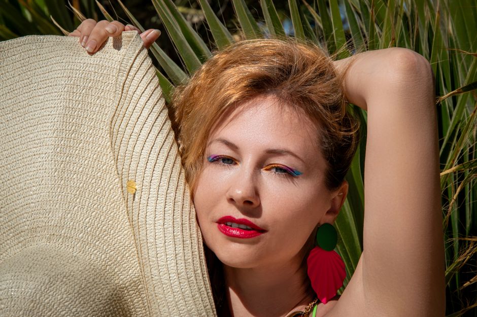 Chic woman with bold makeup poses with a straw hat against palm leaves. Perfect for summer fashion and lifestyle themes.