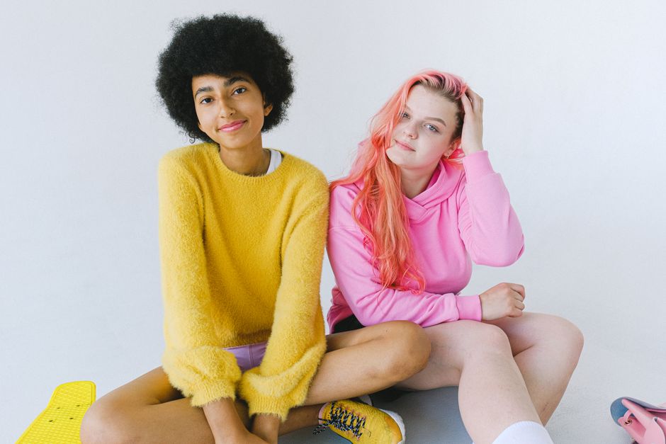 Cheerful multiracial teenagers with unusual haircuts smiling and looking at camera on white background of studio