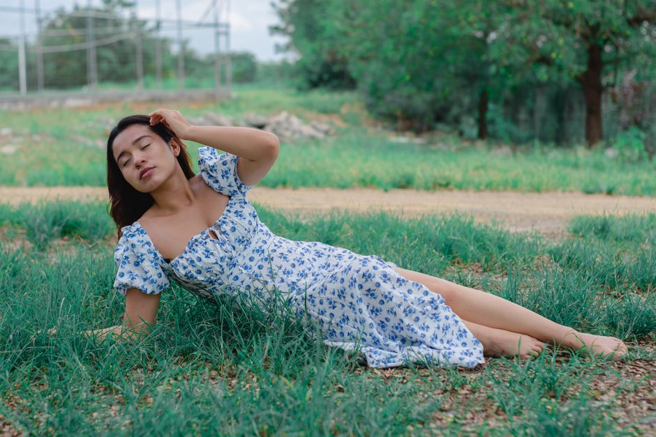 A serene moment of a woman in a blue floral dress lying on grass in a summer field.