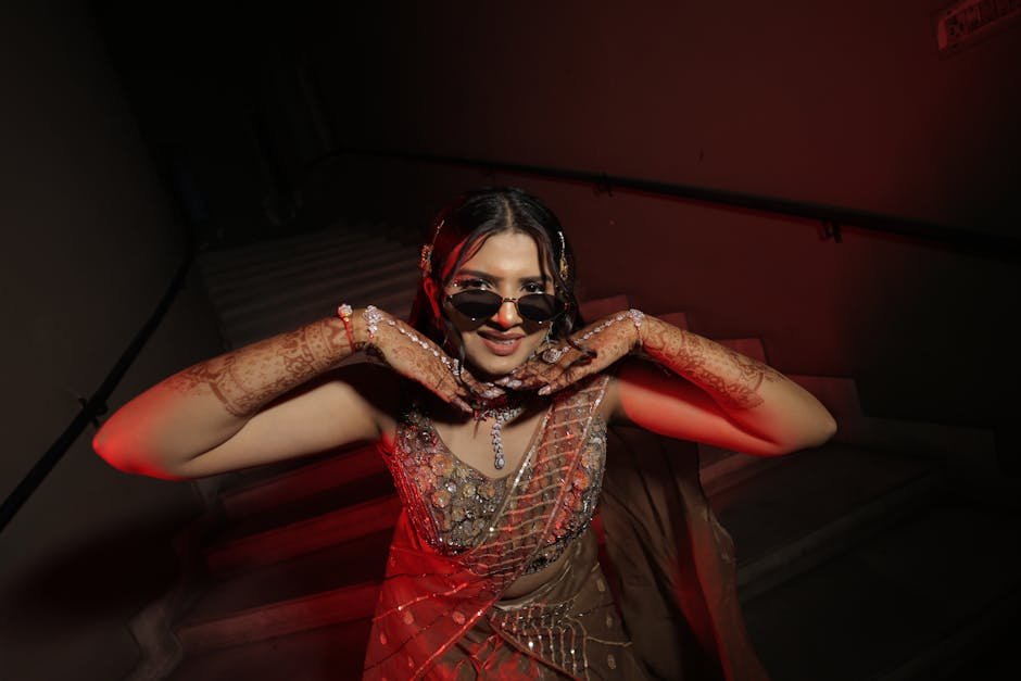 Elegant woman in saree poses on stairs with henna design and sunglasses.
