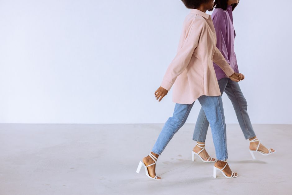 Two women in trendy attire walking against a white background showing modern fashion sense