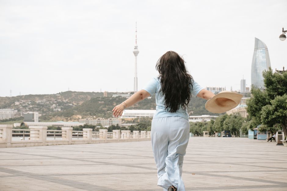 A carefree woman in blue clothing runs towards the Baku skyline, enjoying a sunny outdoor day.