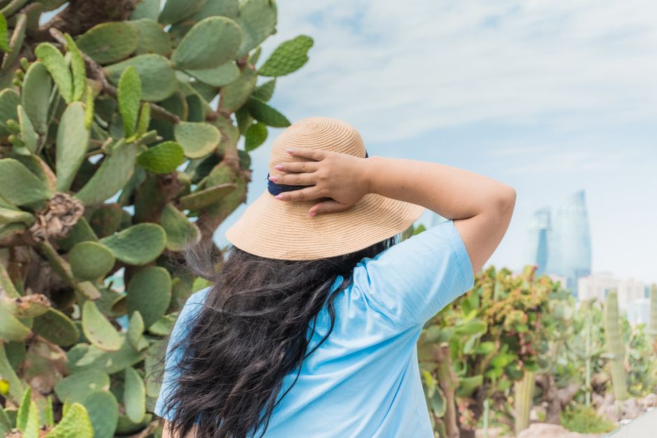 Woman in a straw hat discovering Baku's cacti garden with city skyline view.