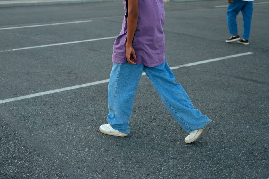 Unrecognizable person walking in a parking lot wearing a purple top and denim jeans.
