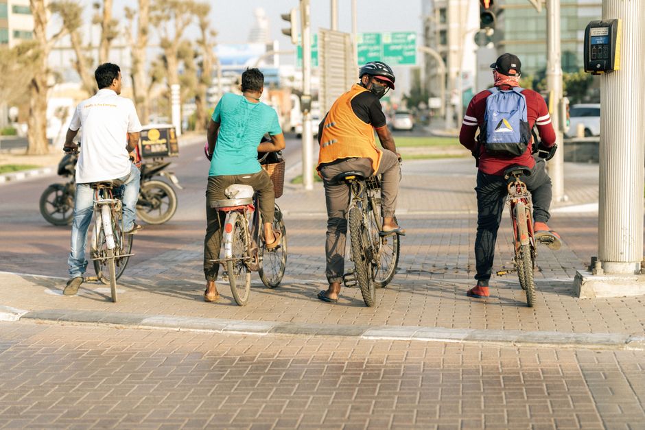 A group of cyclists waiting at a city crosswalk under sunlight, creating an urban scene.