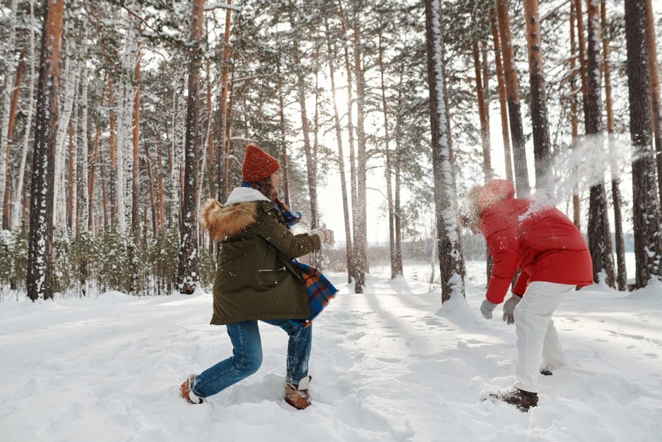 A couple playing joyfully in the snow in a scenic winter forest, creating a lively and warm atmosphere.