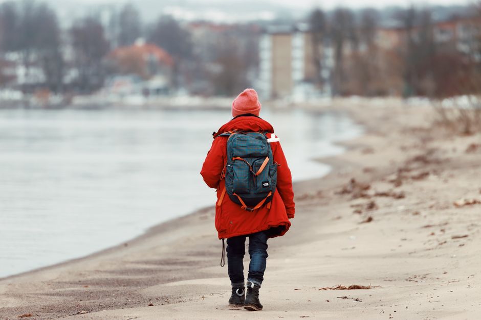 Person in red jacket walks on a Swedish beach in winter, showcasing travel and solitude.
