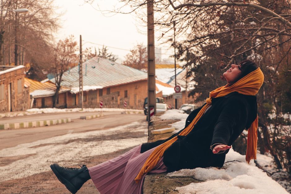 Woman wearing a head scarf sitting outside in a snowy street, embracing winter.