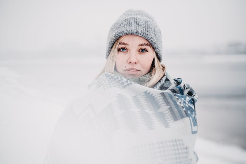 Woman with blue eyes and blonde hair wrapped in a scarf, outdoors in winter.