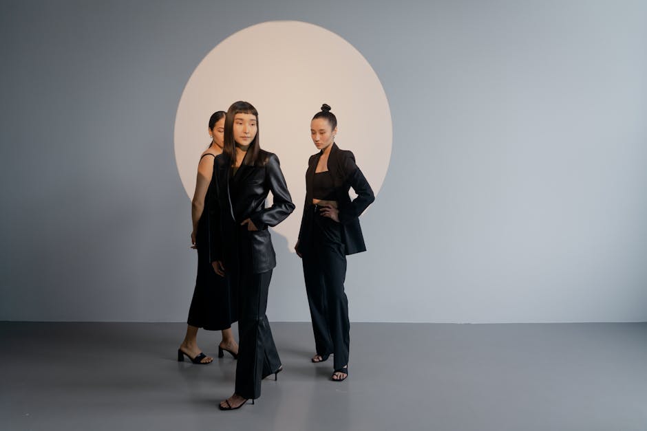 Three Asian women in black outfits pose stylishly in a modern studio with a circular backdrop.
